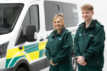 An ambulance with two medical professionals smiling in front of it.