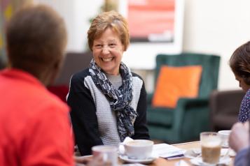 An older woman in conversation with another person, smiling broadly.