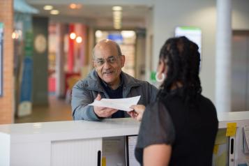 An older man being given a document by a receptionist in a clinical setting.