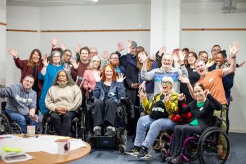 A group photo of a professional team in a conference room with everyone smiling and putting their arms up.