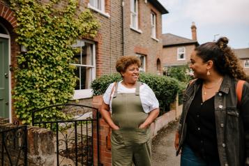 Two women walking together and smiling outside terraced houses.