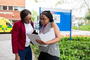 Two women looking at a folder outside a hospital.
