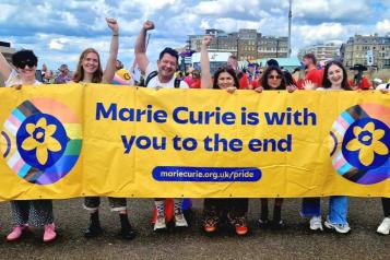 A group photo of a team of Marie Curie employees with a Pride banner and flags.