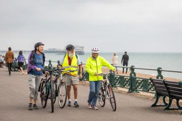 Three people with bikes walking along Brighton seafront.