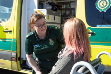 An ambulance professional talking to a service user in front of an ambulance.