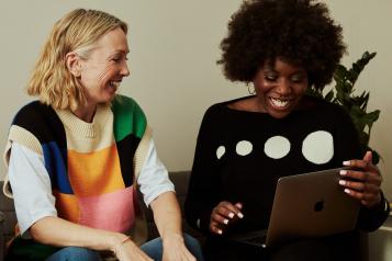 Two women looking at a computer and laughing on a sofa
