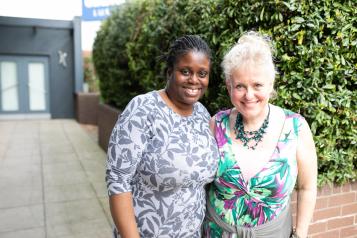 Two women smiling together outside a building. 
