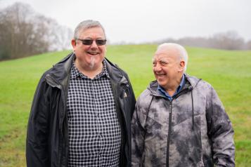 Two older men smiling next to each other in a field.