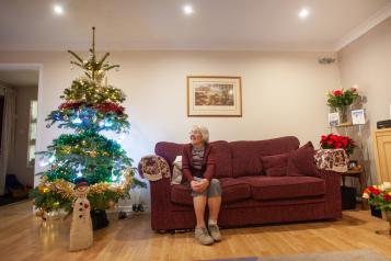 Older woman sat on sofa looking at Christmas tree