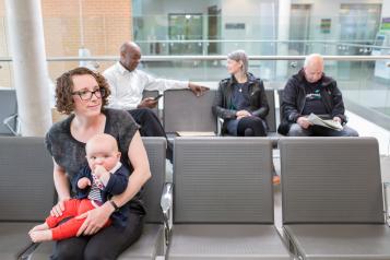 A woman and her baby seated in a clinical waiting room.