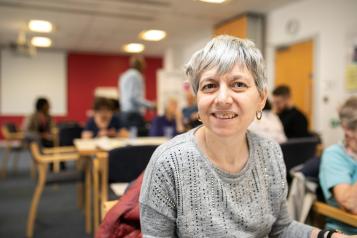 A woman smiling sat at a table in an indoor setting.