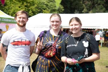 Three young people outside in a sunny, festival environment.
