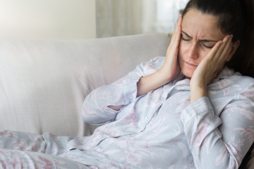 Woman lying on sofa and holding head as if in pain.