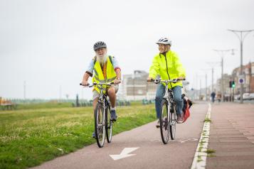 Two older adults cycling together along Brighton seafront.