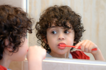 Child looking in mirror while brushing their teeth.