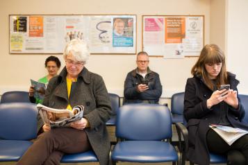 Several people, male and femail, older and younger, in a doctors waiting area.