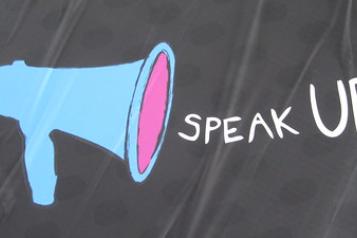 Blue microphone to the left hand side, Speak Up in white writing centrally aligned