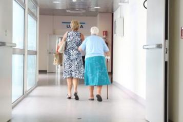 Hospital corridor, Old woman walking arm in arm with a woman, backs to camera