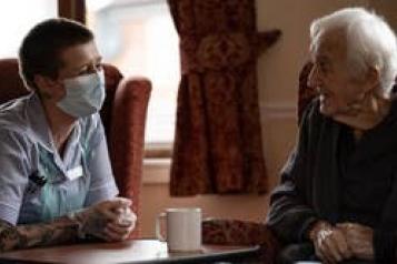 Elderly man and nurse chatting in care home 