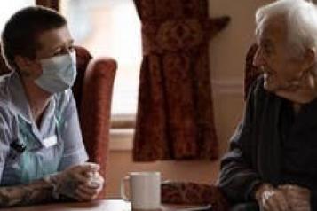 A masked carer talking to an older person 