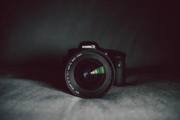 Black backdrop, Canon camera centrally framed, Lens in focus, Background blurred