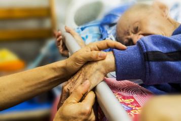 Elderly man in hospital bed, close up of hand being held