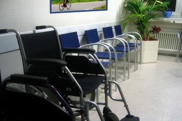 Photograph, wheelchair at front left of image, row of blue chairs alongside