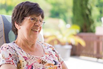 older woman sitting in chair by a garden smiling