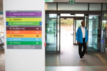 Man standing in hospital next to signage.