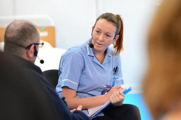 Female nurse, facing towards patient, patient out of focus and at forefront of image