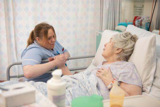 Older woman receiving bedside care in hospital.