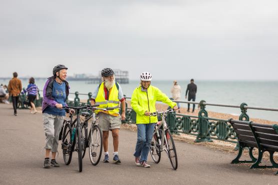 Three people with bikes walking along Brighton seafront.