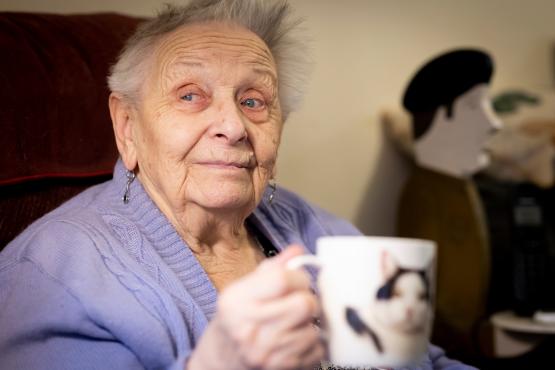 An older woman holding a mug with a cat on it.
