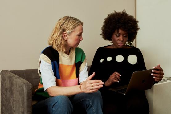 Two women on sofa looking at a laptop together 