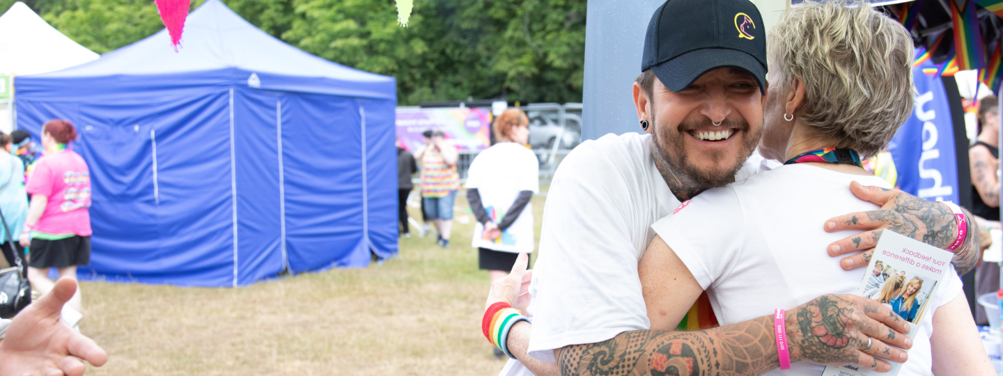 Two people hugging at a Pride festival event outside.