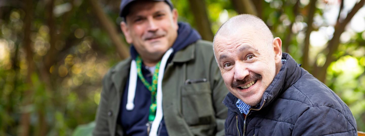 Two men sat outside smiling together.