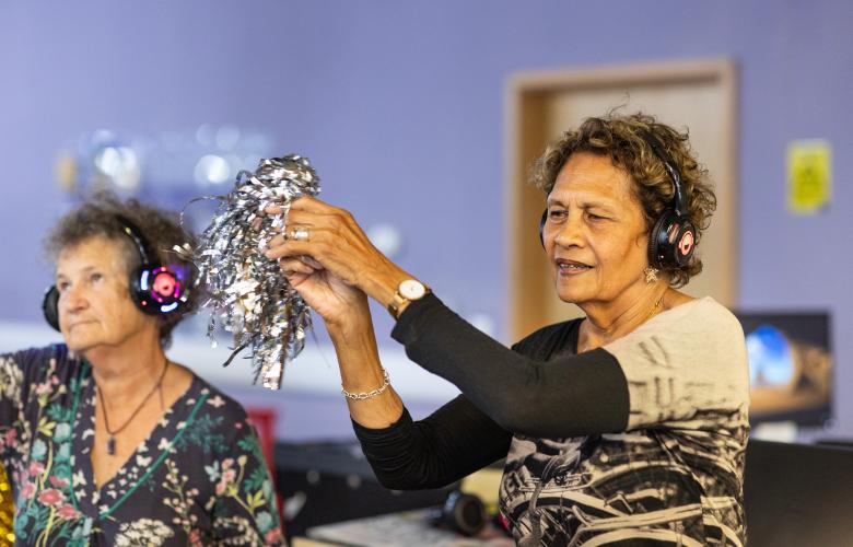 Two older women taking part in a creative dance exercise indoors.