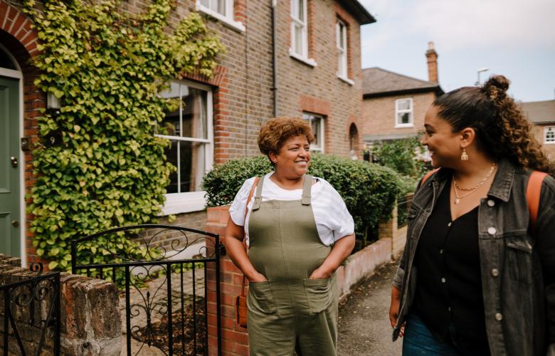 Two women walking together and smiling outside terraced houses.