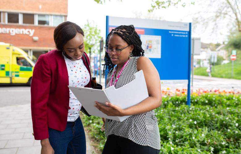 Two women looking at a folder outside a hospital.