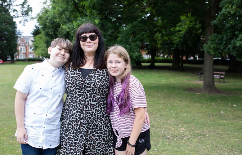 A woman and two children standing together in a park and smiling.