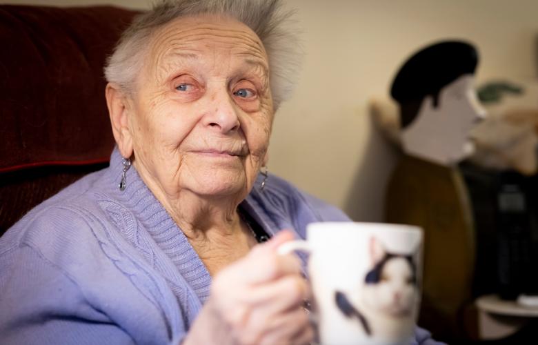 An older woman holding a mug with a cat on it.