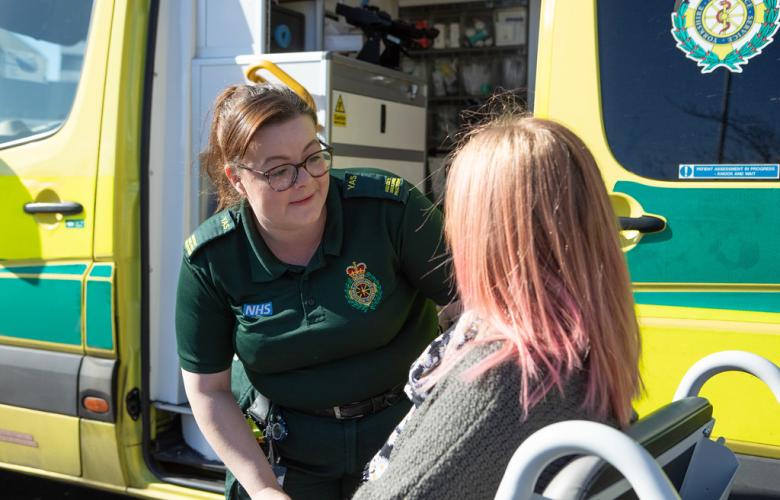 An ambulance professional talking to a service user in front of an ambulance.