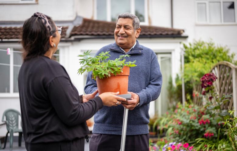 Older man receiving a potted plant from a woman in a garden.