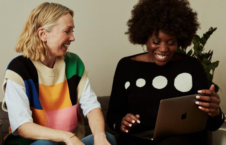 Two women looking at a computer and laughing on a sofa