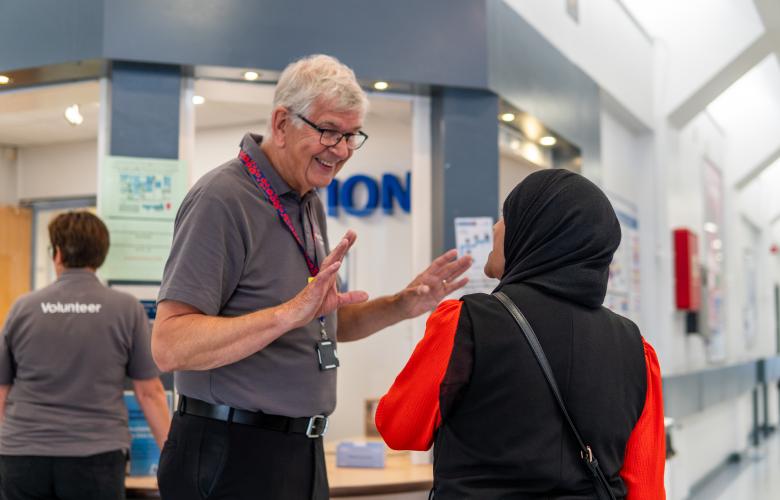 A volunteer speaking to a service user in the corridor of a hospital.