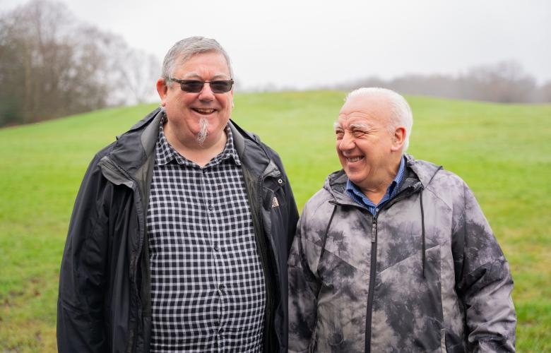 Two older men smiling next to each other in a field.