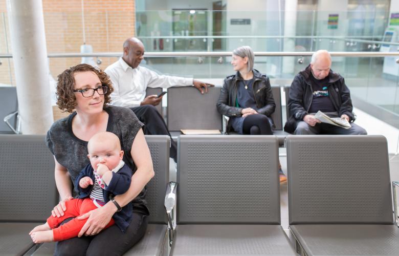 A woman and her baby seated in a clinical waiting room.