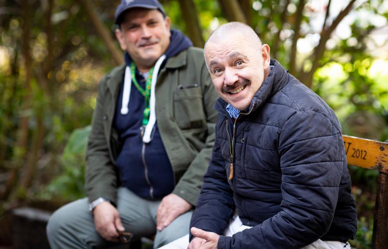 Two men sat outside smiling together.