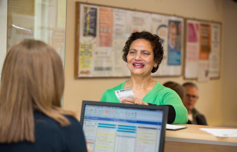 Woman talking at a GP reception counter.