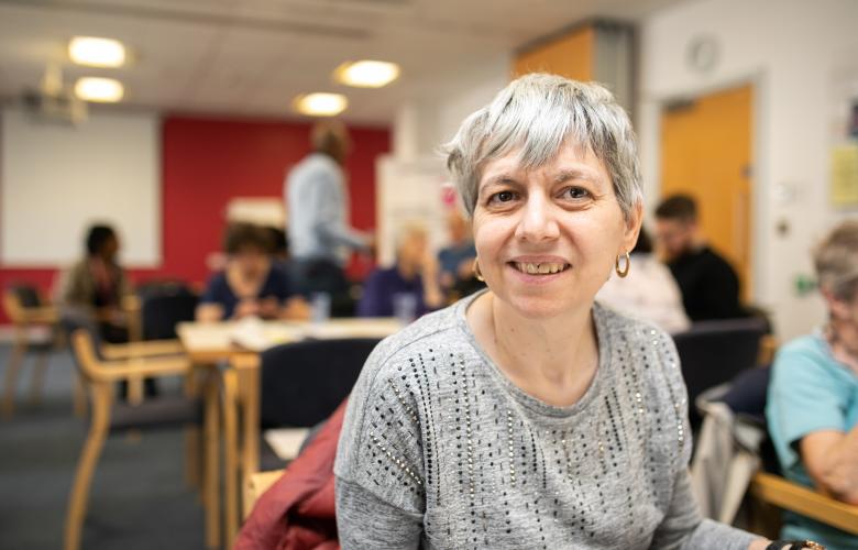 A woman smiling sat at a table in an indoor setting.